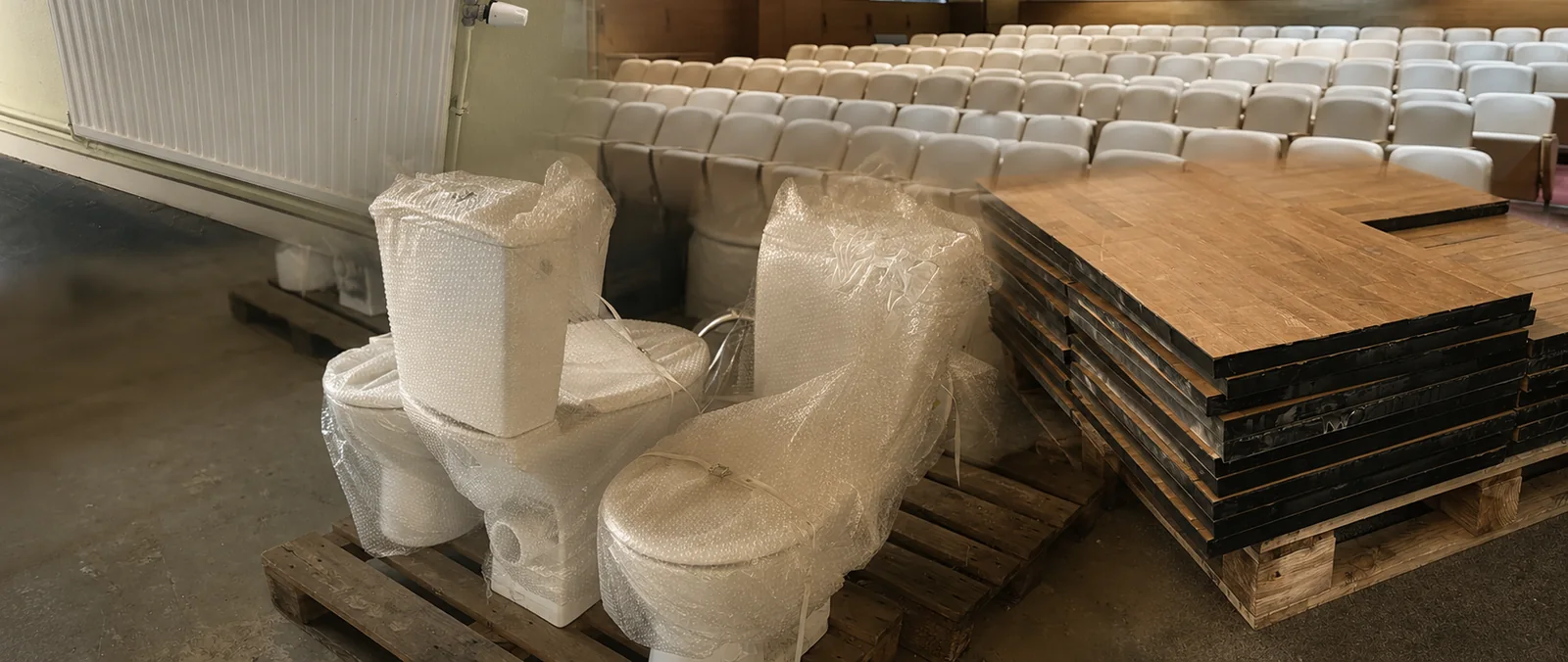 Appareils sanitaires emballés, radiateur et lames de parquet massif déposés et palettisés dans une salle en cours de curage.